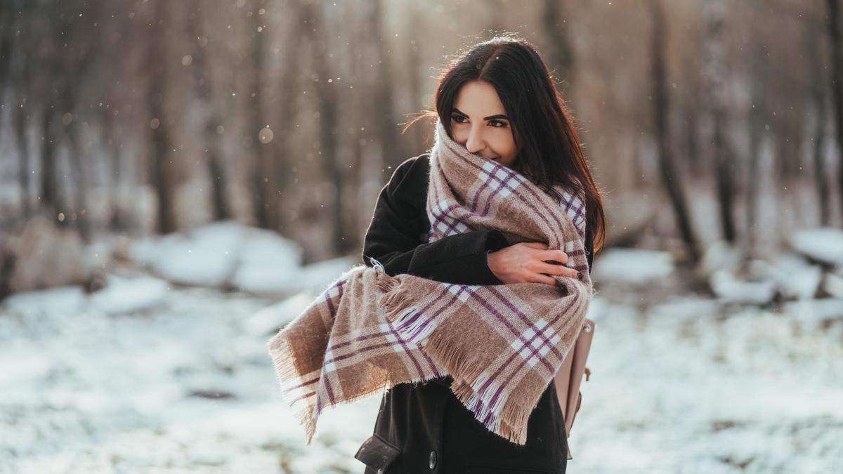 Una mujer se arropa con una bufanda manta en un paisaje nevado.