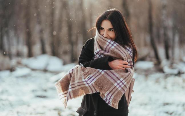 Una mujer se arropa con una bufanda manta en un paisaje nevado. Una mujer se arropa con una bufanda manta en un paisaje nevado.