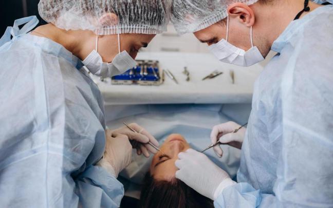 Un cirujano y su asistente realizan una cirug&iacute;a facial.