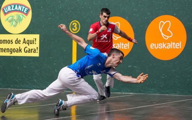 Beñat Rezusta, en una postura acrobática, golpea la pelota ante la mirada de Joseba Ezkurdia. Beñat Rezusta, en una postura acrobática, golpea la pelota ante la mirada de Joseba Ezkurdia.