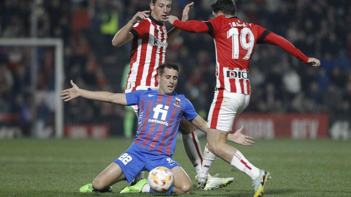 Oier Zarraga, con Mikel Vesga de fondo, golpea el balón ante la oposición de Juanto Ortuño.