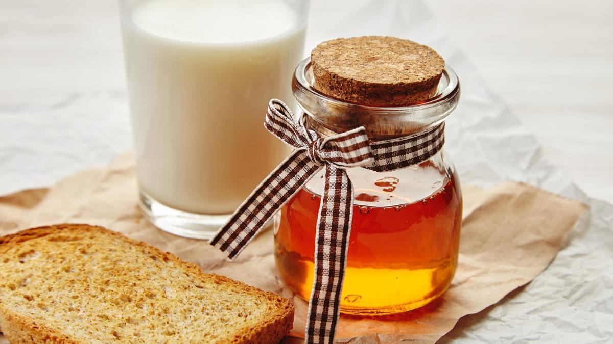 Un vaso de leche junto a un tarro de miel.