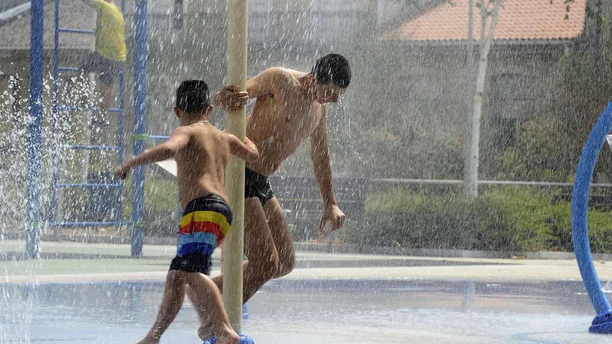 Dos personas se refrescan en unos chorros durante un día de la segunda ola de calor del verano.