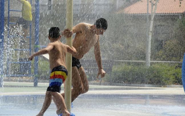 Dos personas se refrescan en unos chorros durante un día de la segunda ola de calor del verano.