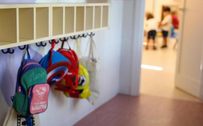 Varias mochilas colgadas en una percha de un aula.