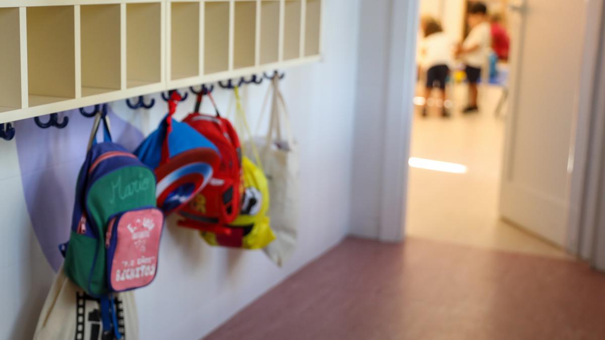 Varias mochilas colgadas en una percha de un aula.