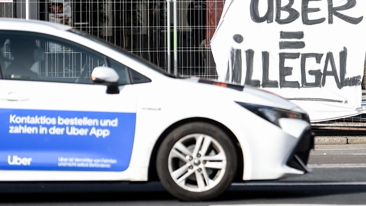 Un Uber pasa por delante de una pancarta, en Berlín, en la que se tacha a la firma de ilegal.