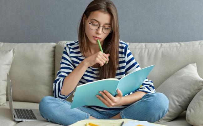 Una joven mira unos apuntes sentada en el sof&aacute;.