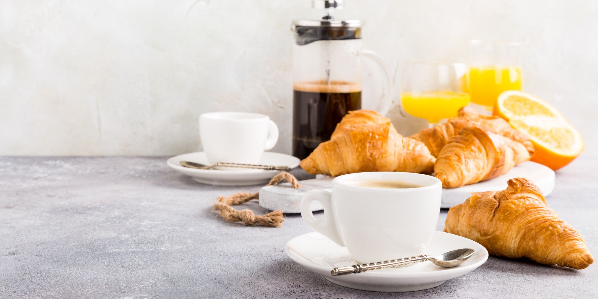 Dos tazas de café y dos zumos de naranja con varias piezas de bollería.