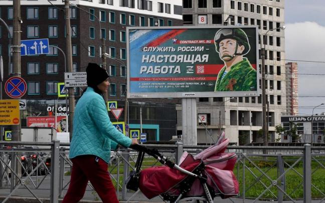 Una mujer pasea en Mosc&uacute; ante un cartel que promociona el servicio militar por contrato.