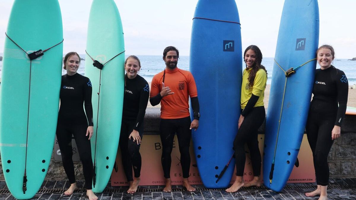 El monitor de Bera Bera Surf Eskola posa junto a sus alumnas con las tablas de surf en la puerta de la escuela.