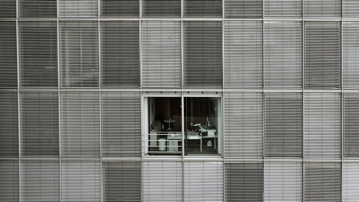 Un hombre trabajando en un despacho con las persianas levantadas.