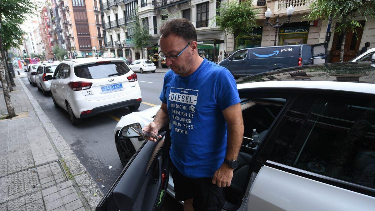 Un taxista mira su móvil mientras espera con su vehículo en la parada sita cerca de la plaza Zabalburu.