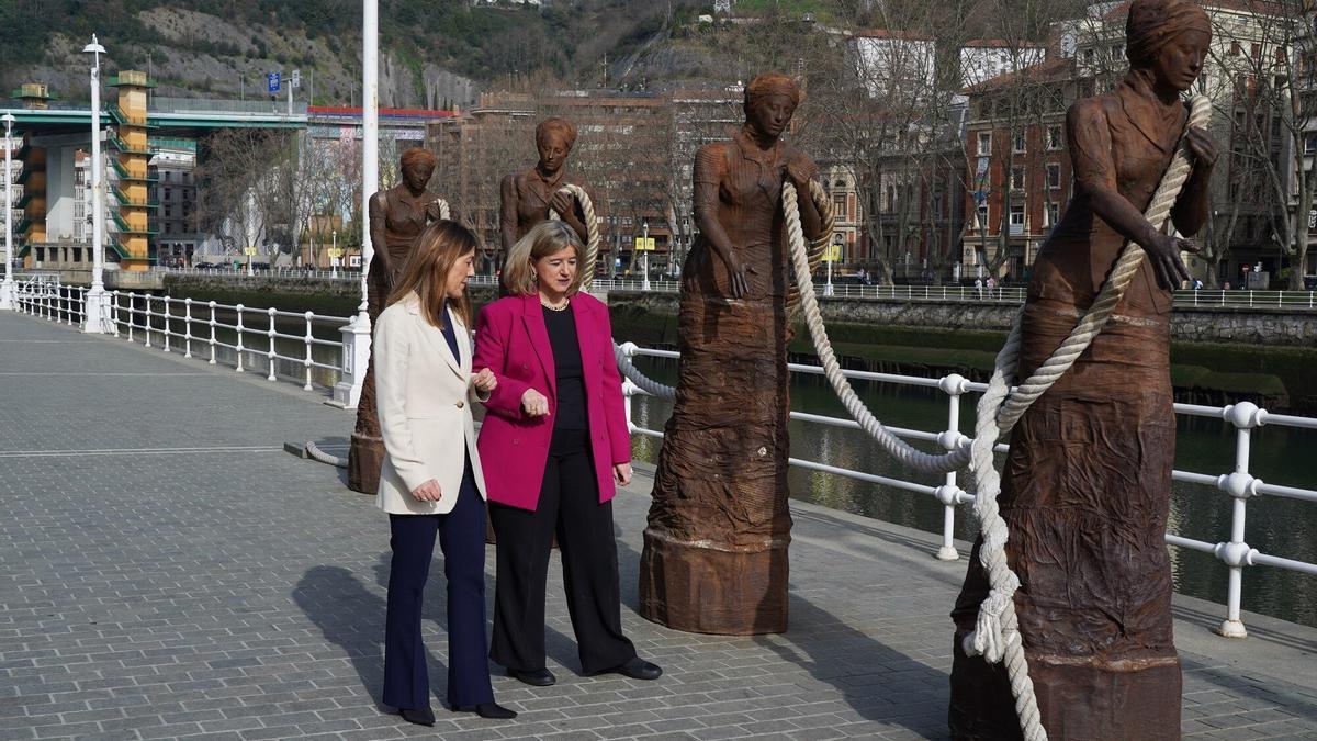 Nora Sarasola junto a Teresa Laespada pasando por delante del conjunto escult&oacute;rico dedicado a las sirgueras.