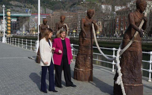 Nora Sarasola junto a Teresa Laespada pasando por delante del conjunto escult&oacute;rico dedicado a las sirgueras.