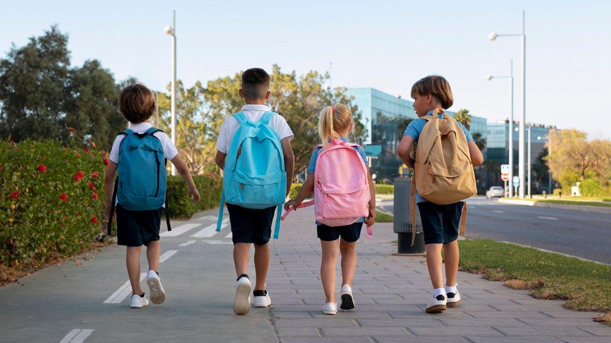 Tres niños y una niña van al colegio con la mochila a la espalda.