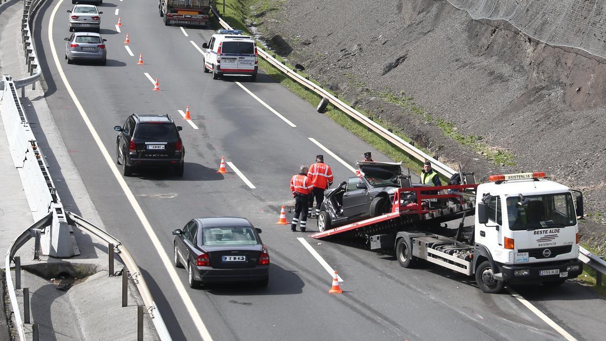 Un agente de la Unidad de Tráfico de la Ertzaintza regula el tráfico mientras la grúa retira un vehículo accidentado.