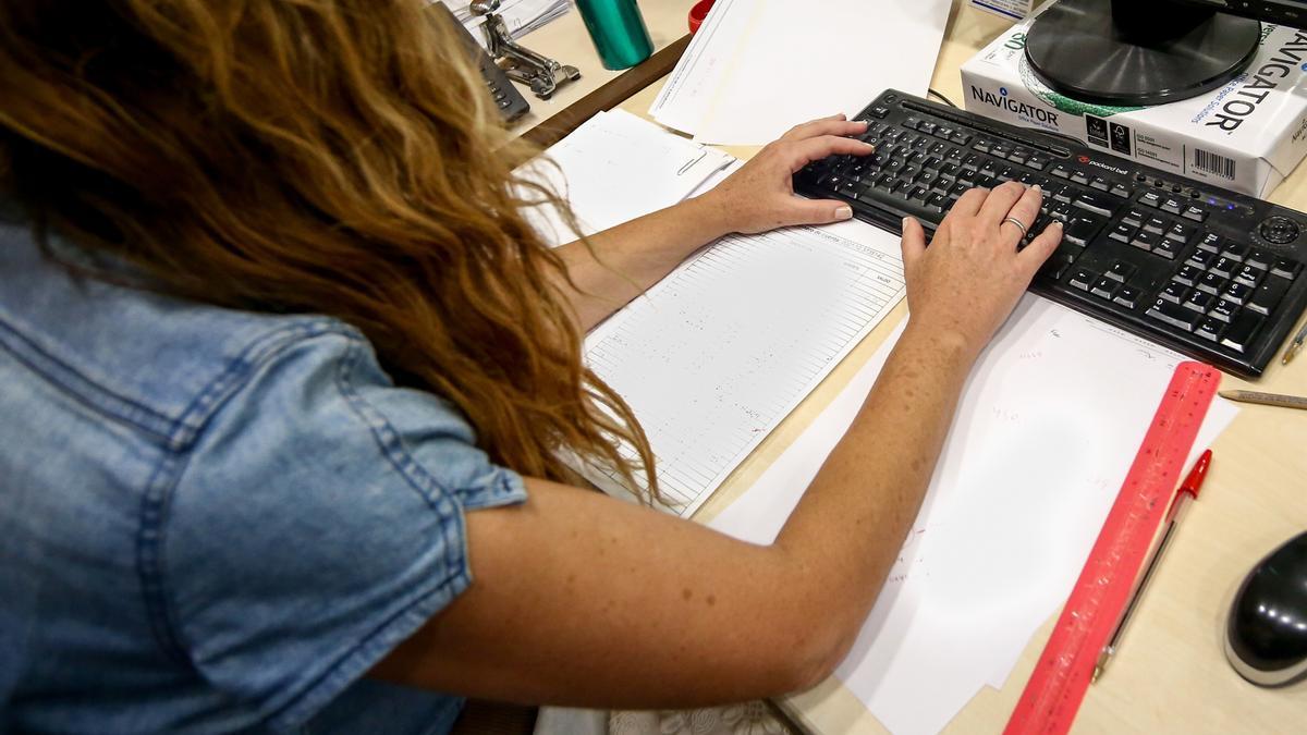 Una mujer escribe en el teclado de su ordenador, con papeles alrededor mientras trabaja en la oficina.