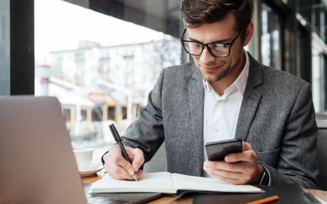 Un hombre con gafas trabaja con su teléfono y su ordenador en la oficina. Un hombre con gafas trabaja con su teléfono y su ordenador en la oficina.