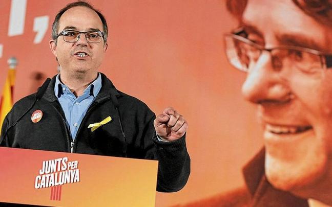 Jordi Turull se dirige a la militancia en un mitin con un cartel de fondo con la figura de Carles Puigdemont.
