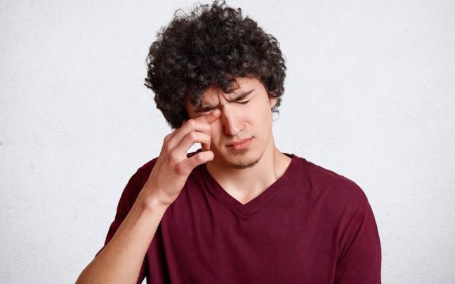 Un hombre se frota el ojo derecho.