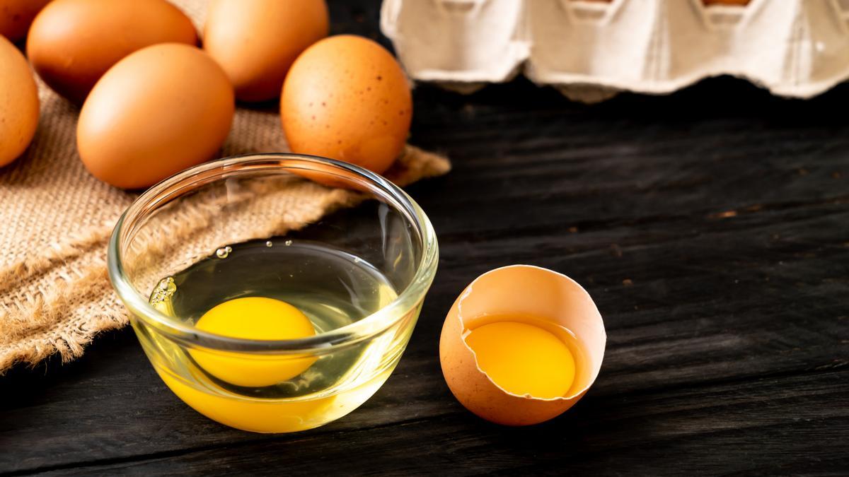 Huevos cascados con la clara y la yema a la vista junto a otros sin cascar.