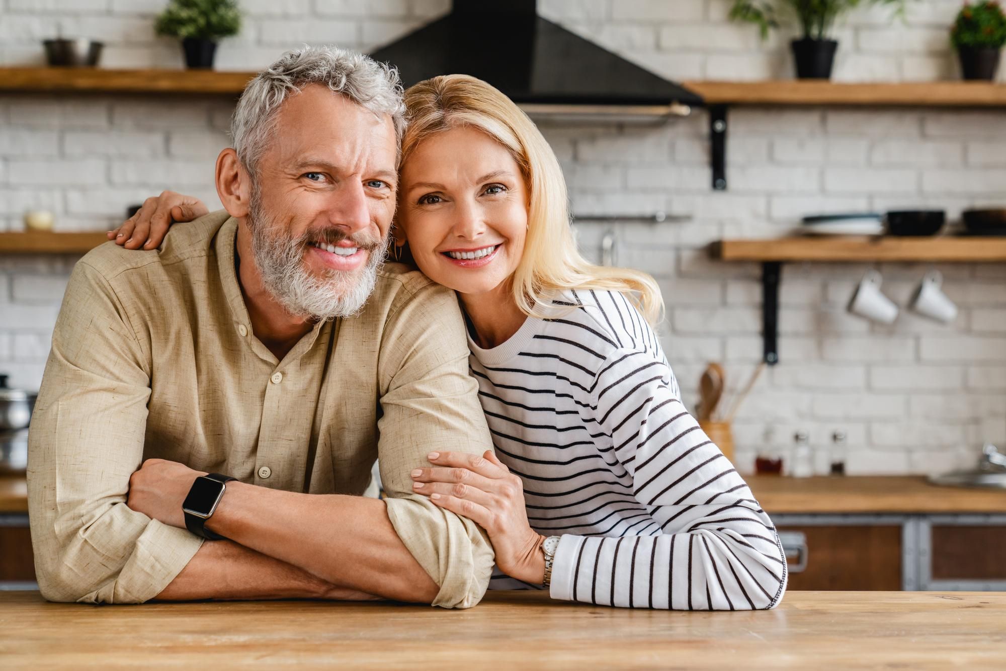 Una pareja de mediana edad posa en la cocina de su casa.