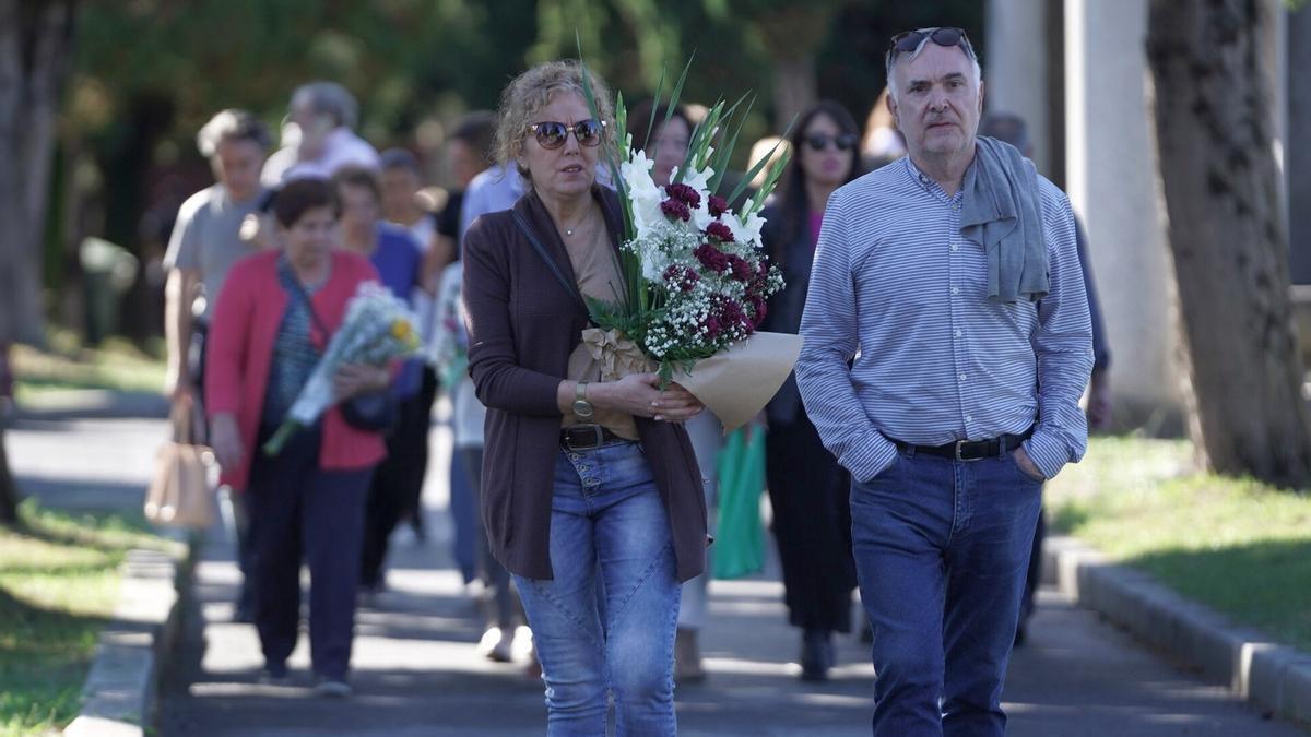 Varias personas caminan con flores por el cementerio de Bilbao.