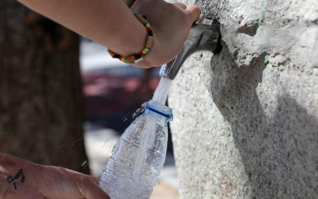 Una mujer rellena una botella de agua en una fuente, en una foto de archivo. Una mujer rellena una botella de agua en una fuente, en una foto de archivo.