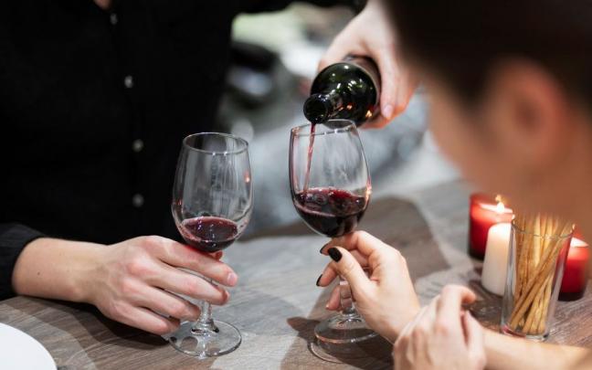 Dos hombres brindan con una copa de vino mientras comparten almuerzo.