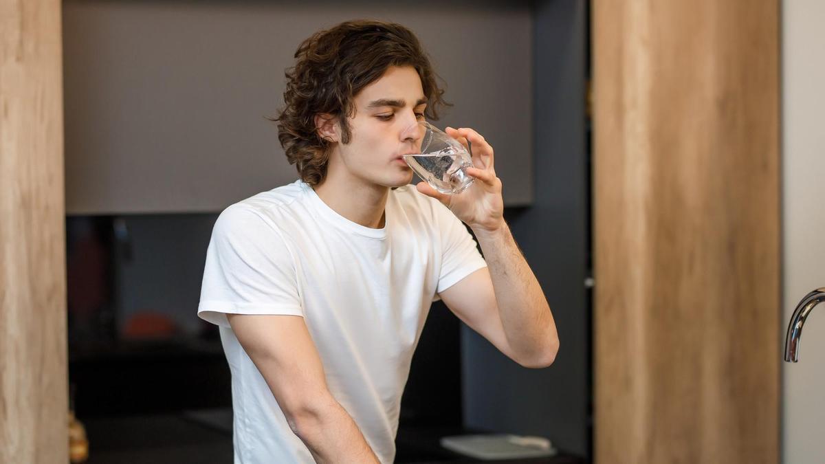 Un joven bebe un baso de agua.