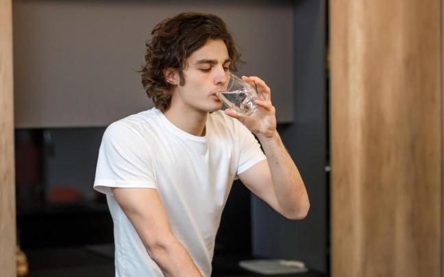 Un joven bebe un baso de agua.