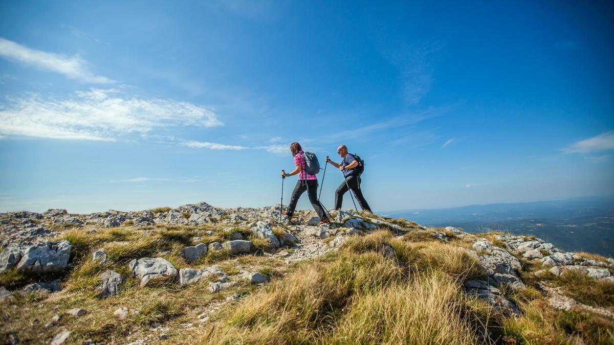 Dos personas se ayudan de palos de trekking para caminar por el monte.