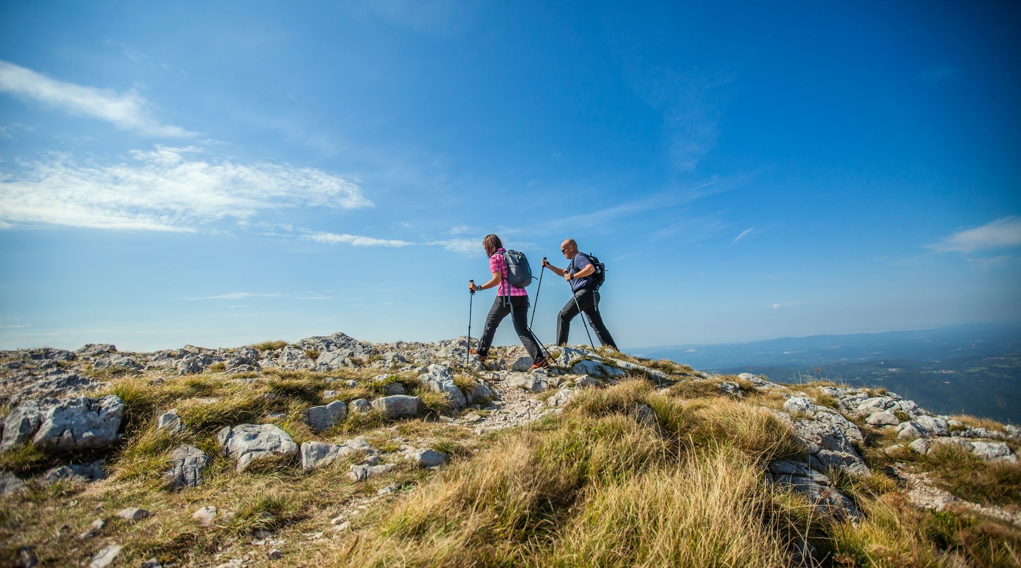 Dos personas se ayudan de palos de trekking para caminar por el monte.