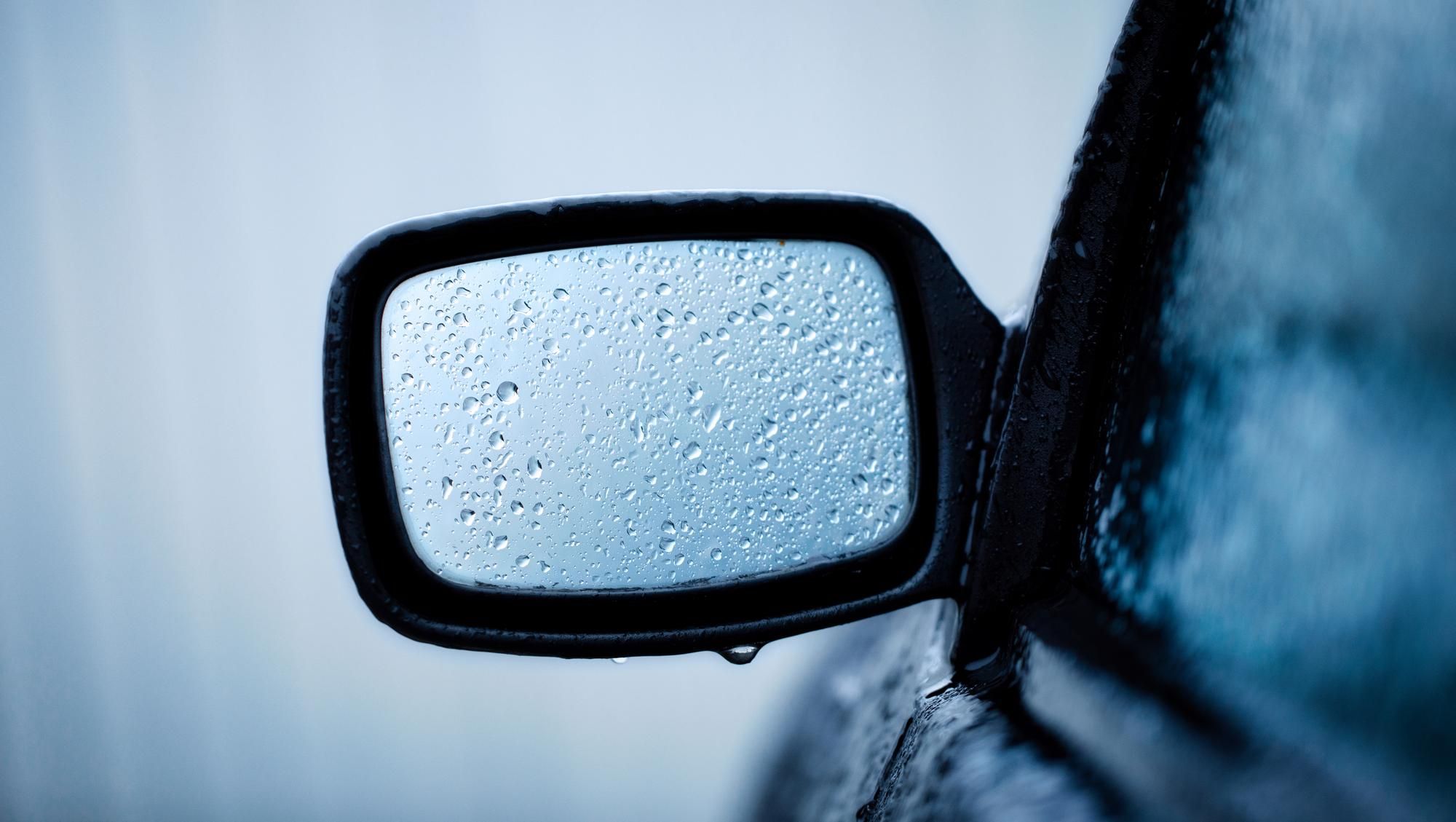 Un espejo retrovisor lleno de gotas de agua en un día de lluvia.