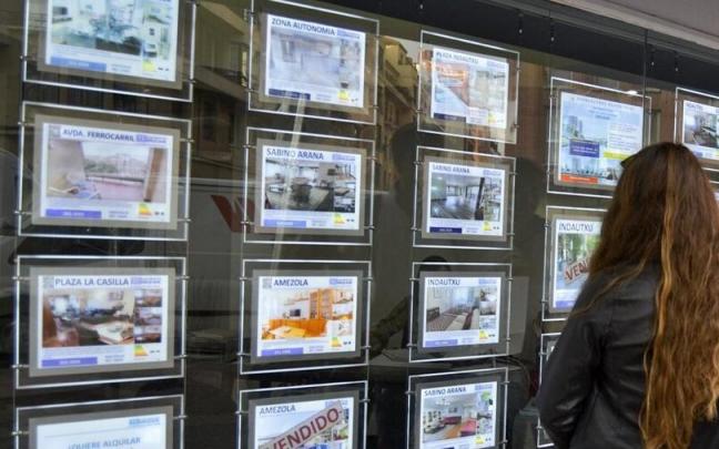 Una joven contempla el escaparate de una inmobiliaria.