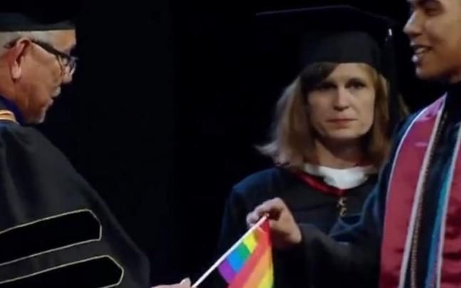 Un estudiante, entregando una bandera arcoíris al rector.