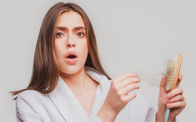 Una mujer sorprendida al ver el cepillo lleno de pelos.