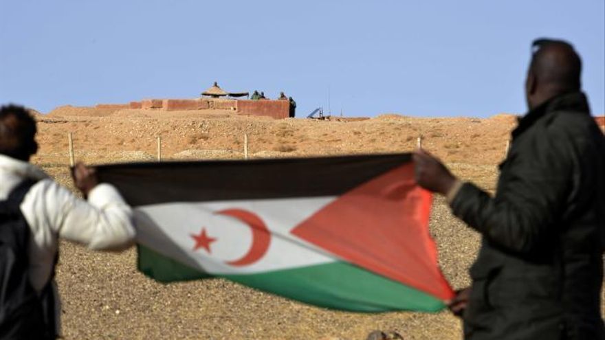 Dos hombres saharauis sostienen una bandera del Frente Polisario al noroeste del paso fronterizo de Guerguera.