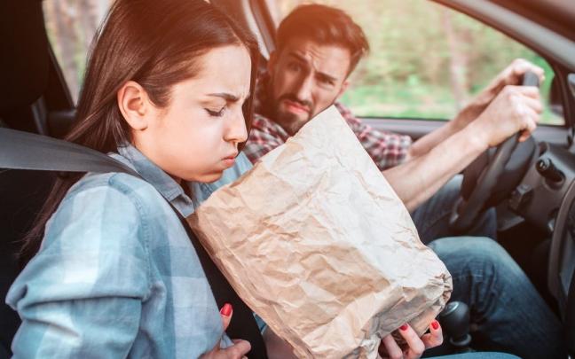 Una mujer vomita en una bolsa tras marearse en el coche.
