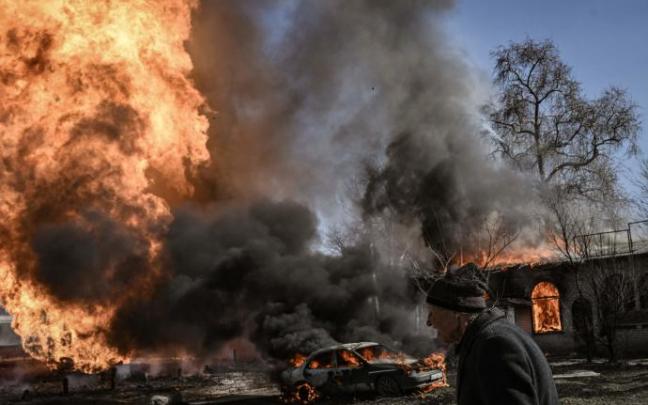 Una mujer camina junto a las llamas y el humo que se eleva en la ciudad de Kharkiv.