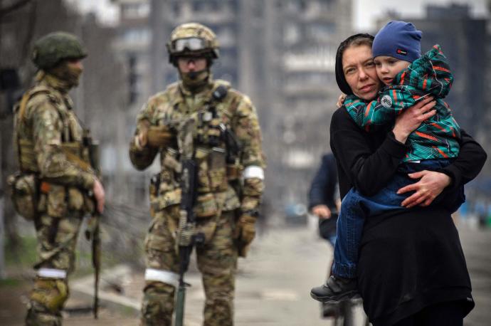 Una mujer abraza a un niño junto a un grupo de soldados rusos en una calle de Mariúpol.