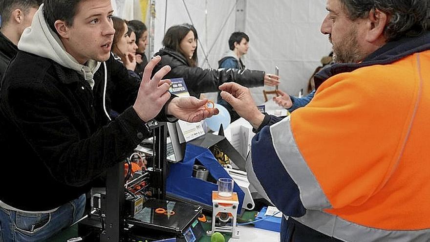 Un estudiante muestra una pieza en su estand a un interesado.