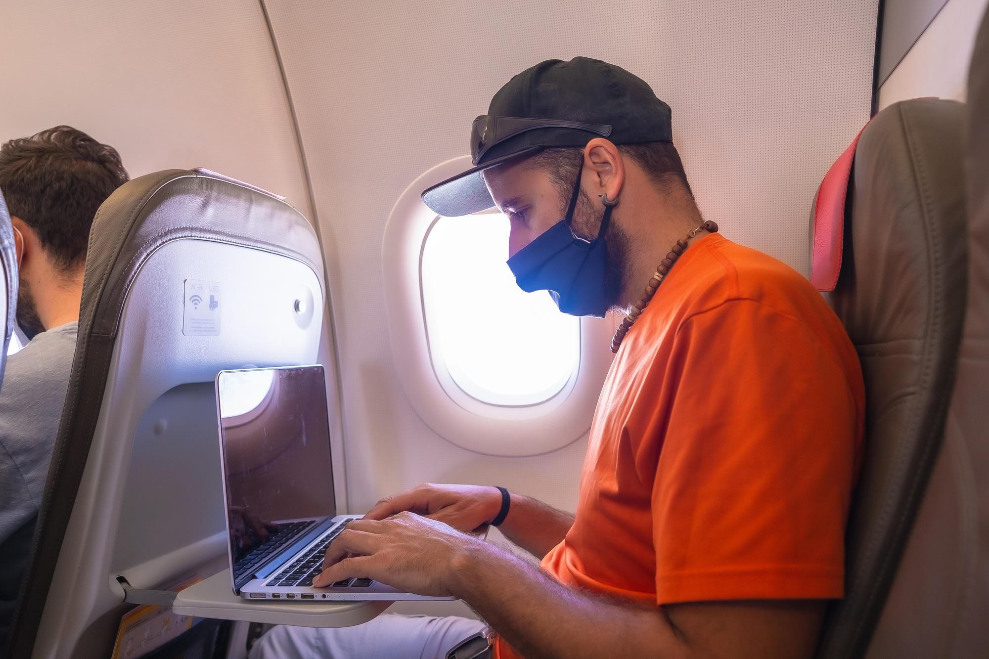 Un hombre con mascarilla maneja su portátil en el avión.