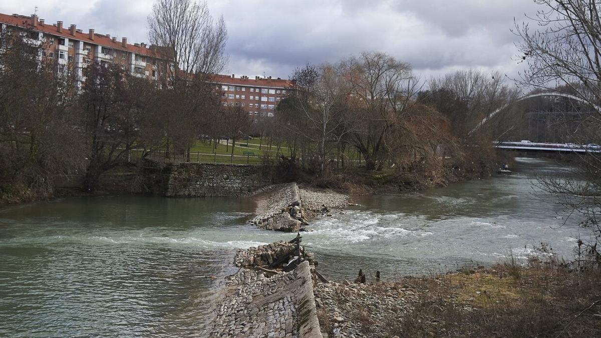 Vista de la presa de Santa Engracia en el río Arga, rota parcialmente desde 2018, y al fondo el puente de Oblatas.