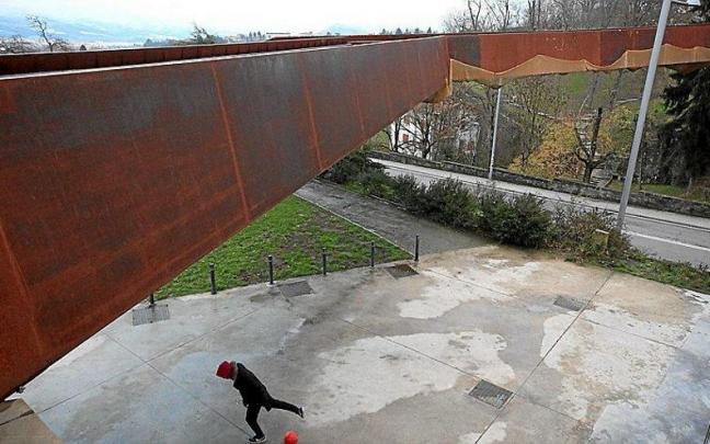 Un niño juega con una pelota junto al frontón debajo la pasarela del Labrit, donde se observa la presencia de una malla colocada para evitar desprendimientos.