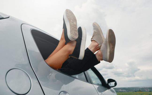 Dos jóvenes sacan los pies por la ventanilla de un coche. Dos jóvenes sacan los pies por la ventanilla de un coche.
