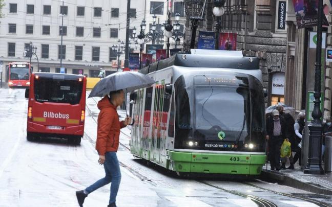 Una persona cruza por una céntrica zona de la capital vizcaina con varias unidades de Bilbobus y el tranvía en las inmediaciones.