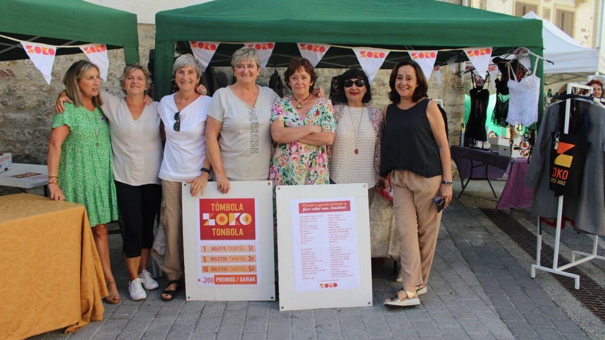 Voluntarias delante de la tómbola y del puesto de ropa de segunda mano posan satisfechas con el desarrollo de la mañana de mercado.