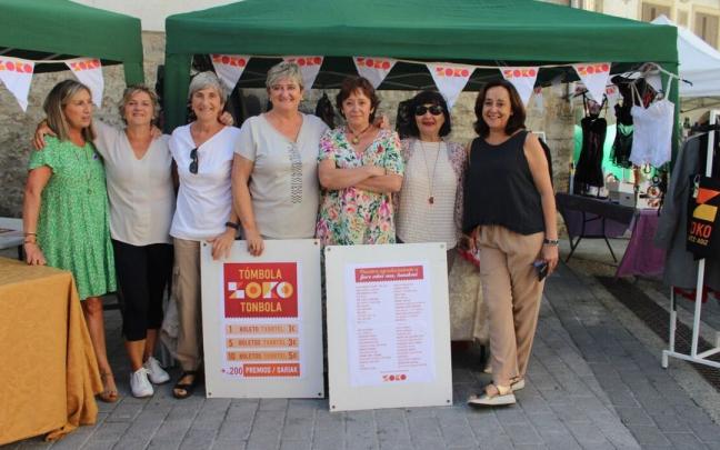 Voluntarias delante de la tómbola y del puesto de ropa de segunda mano posan satisfechas con el desarrollo de la mañana de mercado.